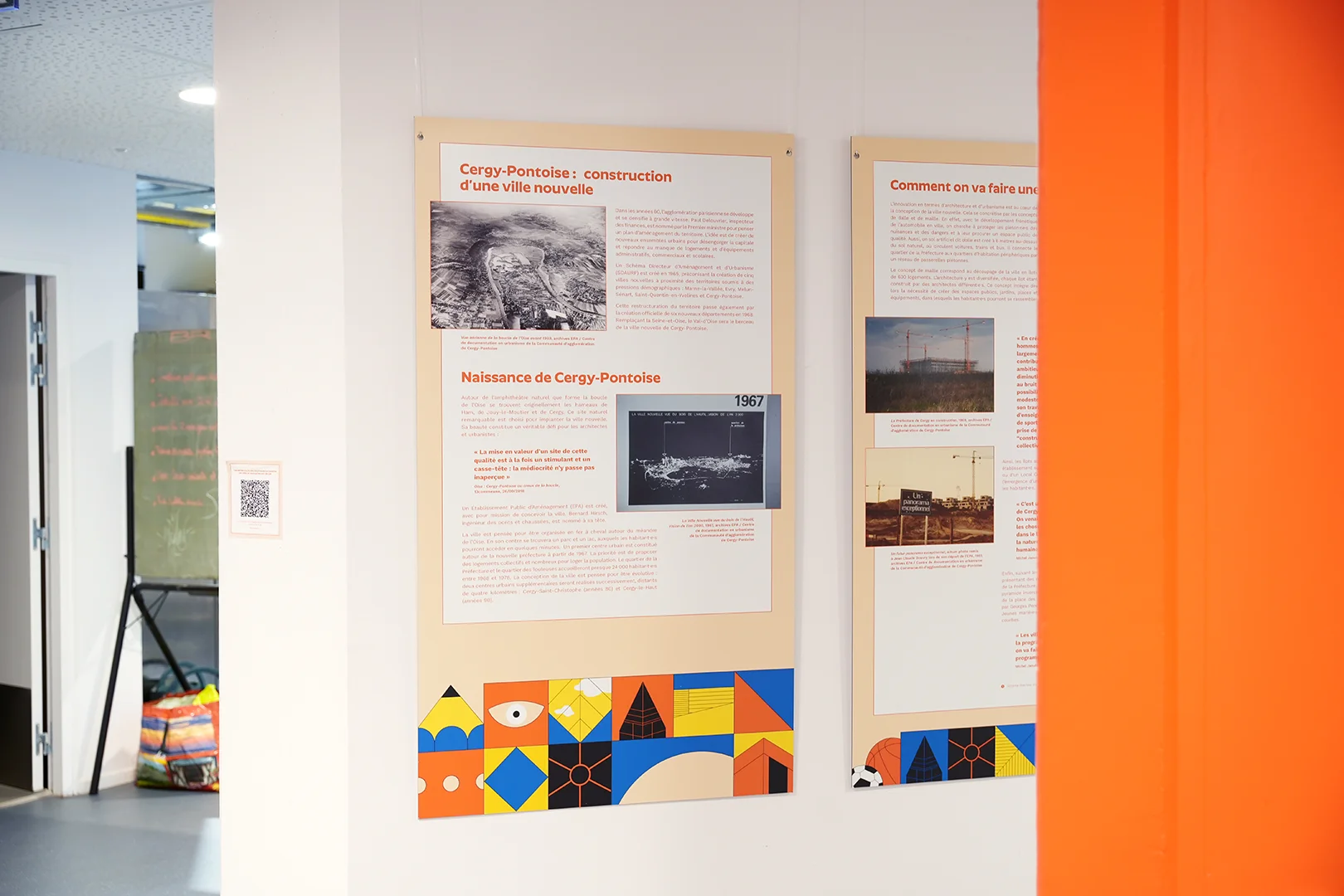 Deux supports installés dans l'exposition, sous la forme de panneaux orangés, avec une frise graphique multicolore en bas. On y lit les titres « Cergy-Pontoise: construction d'une ville nouvelle » et « Naissance de Cergy-Pontoise ». Le panneau de droite est à moitié masqué par un mur orange, en amorce.