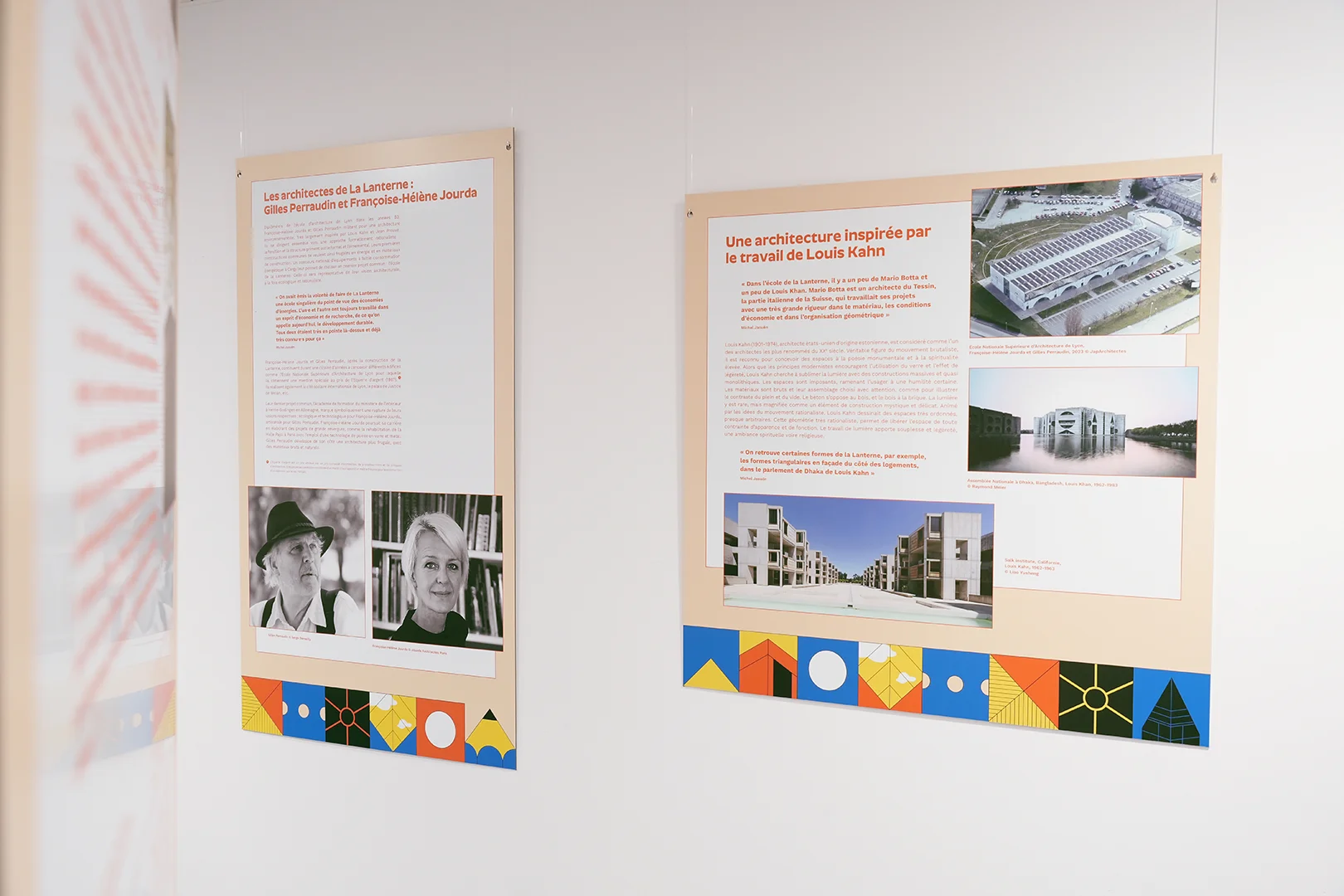 Deux supports installés dans l'exposition, sous la forme de panneaux orangés, avec une frise graphique multicolore en bas. On y lit les titres « Les architectes de La Lanterne: Gilles Perraudin et Françoise-Hélène Jourda » et « Une architecture inspirée par le travail de Louis Kahn ». À gauche, on devine un troisième panneau, à la perpenticulaire.