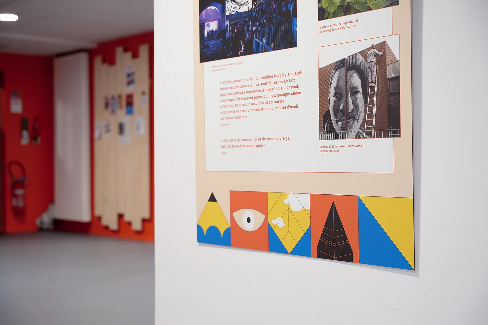 Détail du bas d'un panneau installé dans l'exposition. On distingue particulièrement la frise multicolore qui habille le bas des panneaux : elle est composée de blocs carrés comportant des illustrations dessinées au trait noir (crayon, fenêtre, détail d'architectures, formes géométriques)