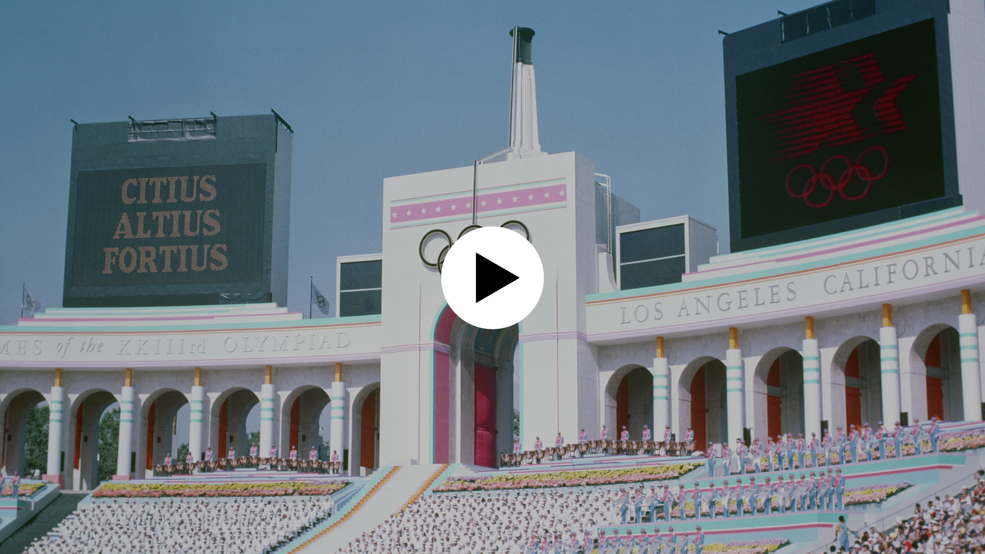 Vue du Coliseum pendant la Cérémonie d'ouverture des Jeux olympiques de Los Angeles 84. Icône play en surimpression indiquant que l'image est cliquable et mène vers un contenu vidéo.