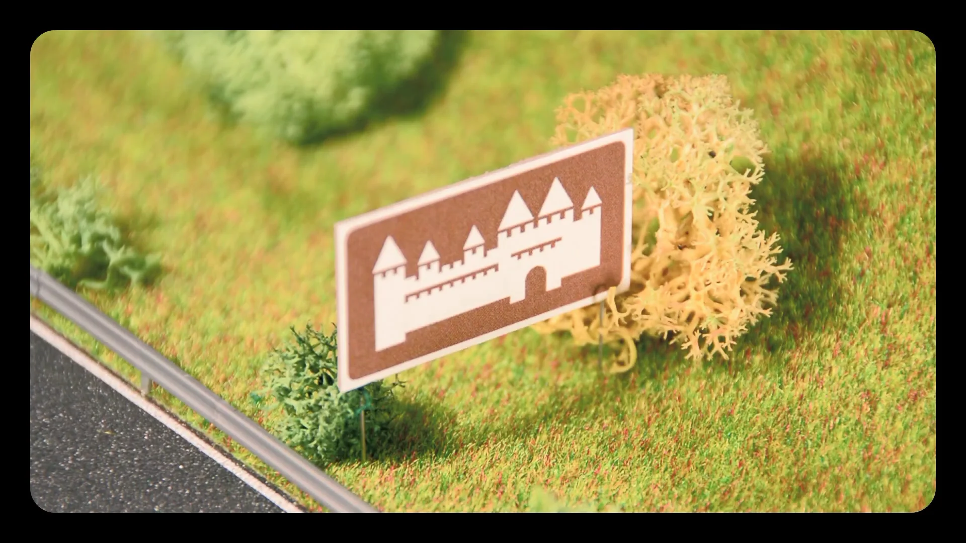 Capture de la vidéo : maquette d'un paysage, avec un panneau marron au bord d'une route.