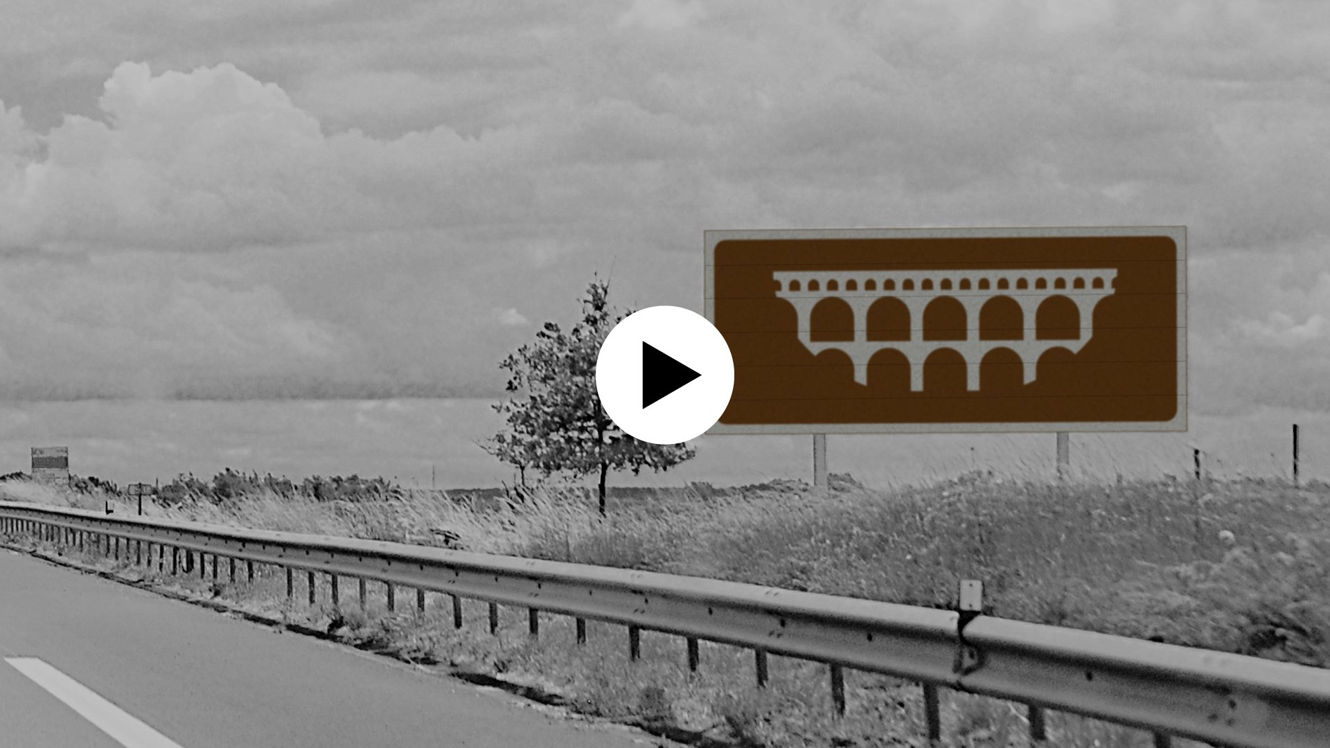Image d'un panneau marron (avec un pictogramme représentant le Pont d'Avignon) au milieu du paysage, en bord de route. Icône play en surimpression indiquant que l'image est cliquable et mène vers un contenu vidéo.